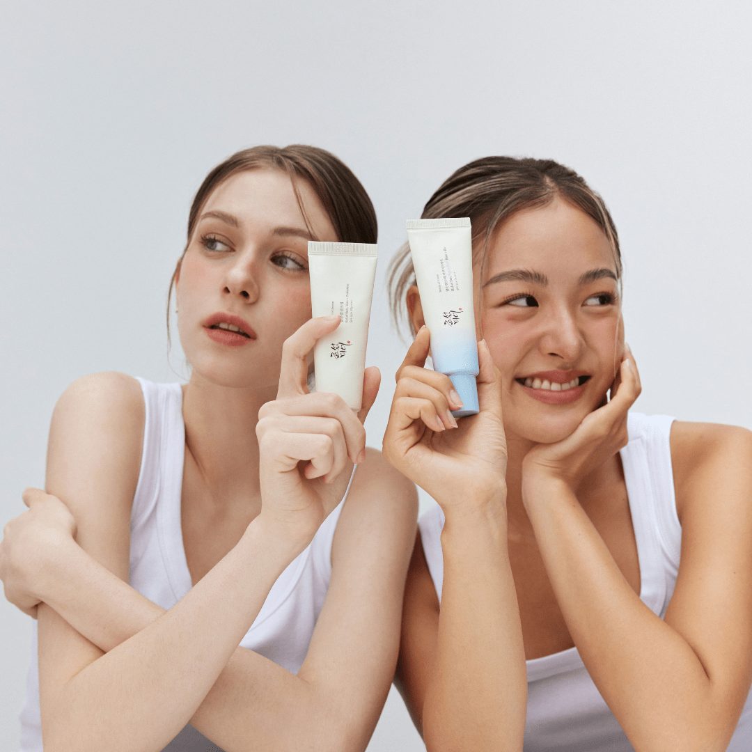 Two women holding skincare products against a plain background